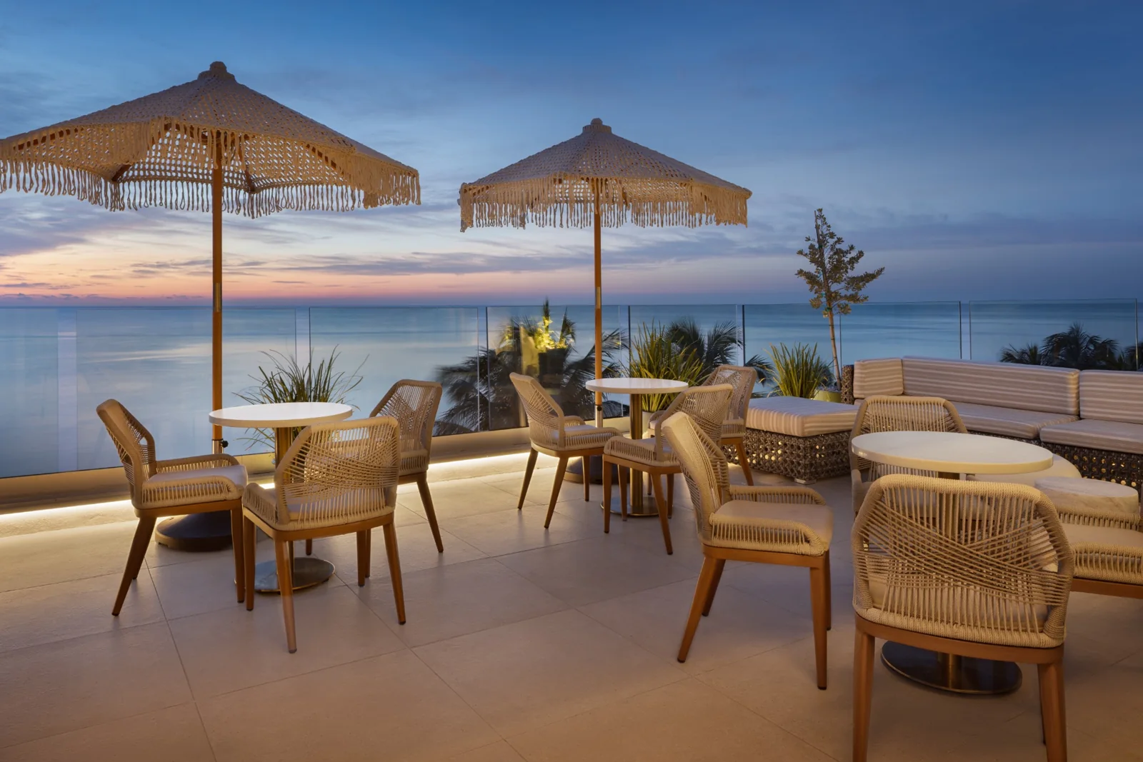 Oceanfront terrace with woven umbrellas and seating at dusk