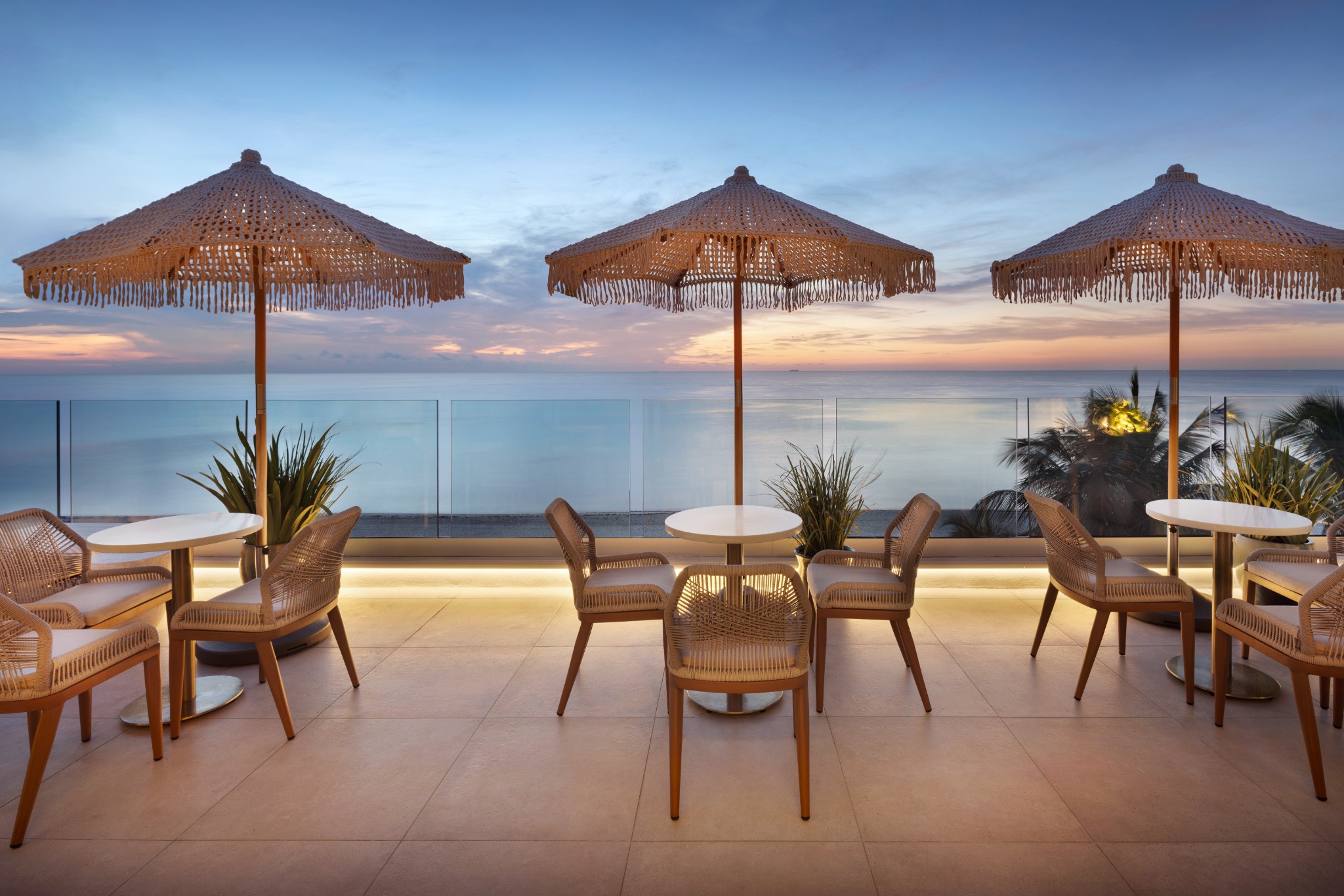 Oceanfront terrace tables beneath woven umbrellas at Kalypso Beach